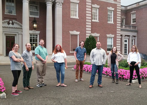 Eight members of the Arts Alumni Group standing outside of Hennessy Hall