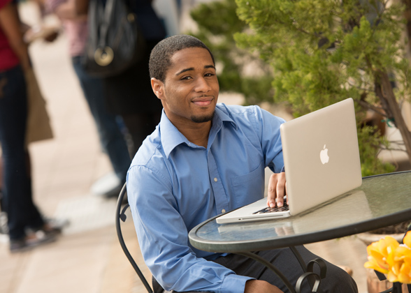 Male student sitting outside at a table working on a laptop
