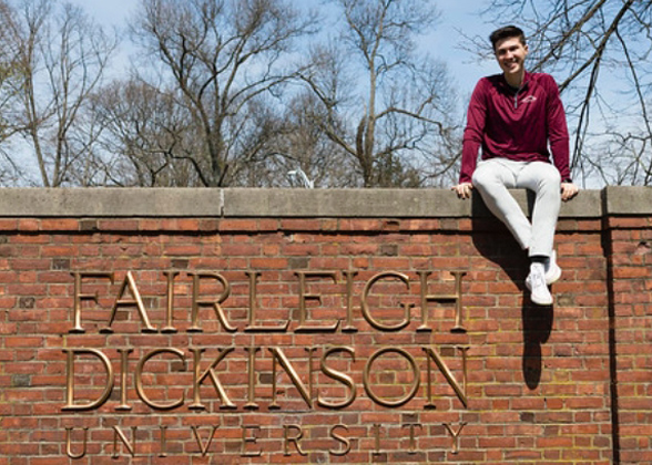 A male student sits on top of the brick wall on Florham Campus.