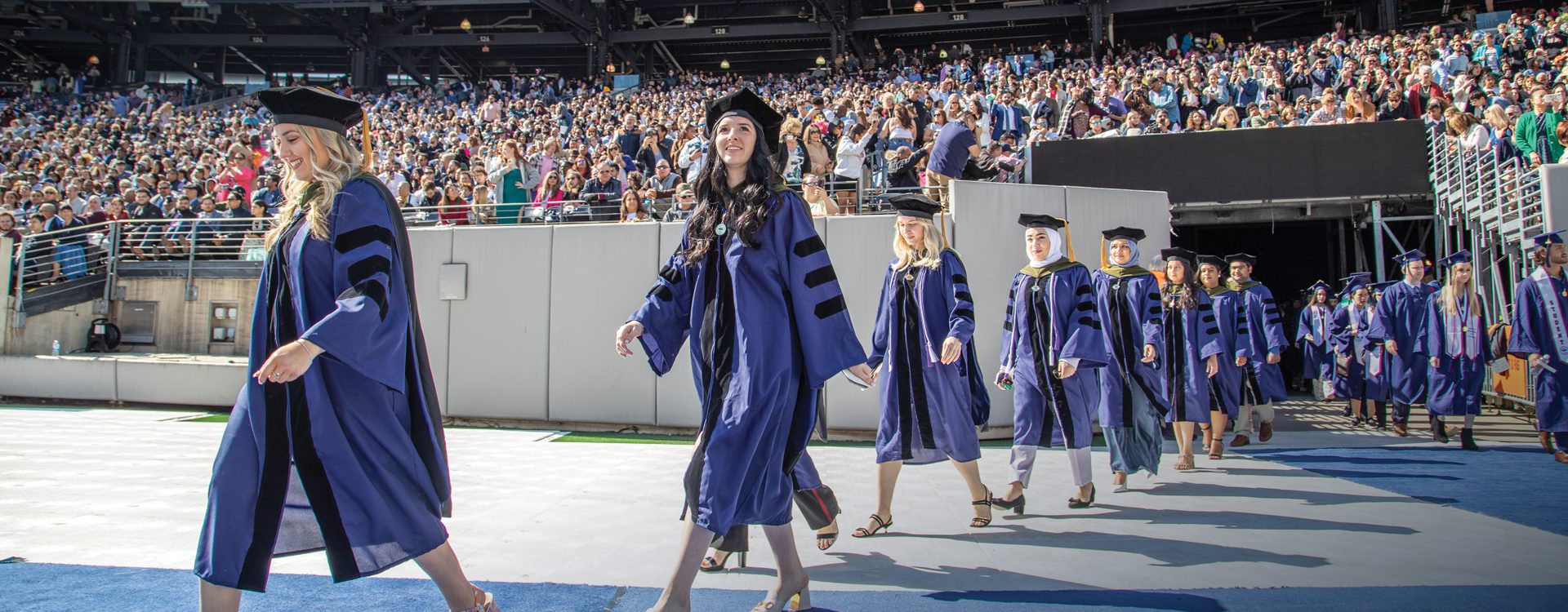FDU graduates walk onto an athletic field during commencement ceremonies.